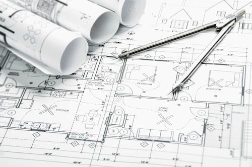 Picture showing the floor plans of a house drawn out on sketching paper, with a drawing compass on top of the stack of papers.