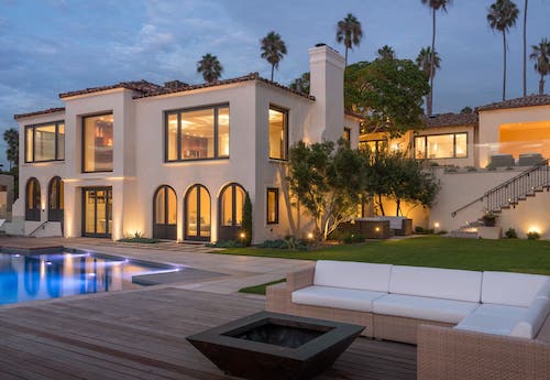 Picture of the outside of a modern-looking, geometrically designed home. There is a pool in the backyard and the sun is setting.