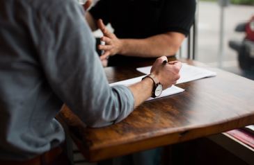 Two people sitting at a table, and using hand gestures implying they are having a discussion and sharing opinions.