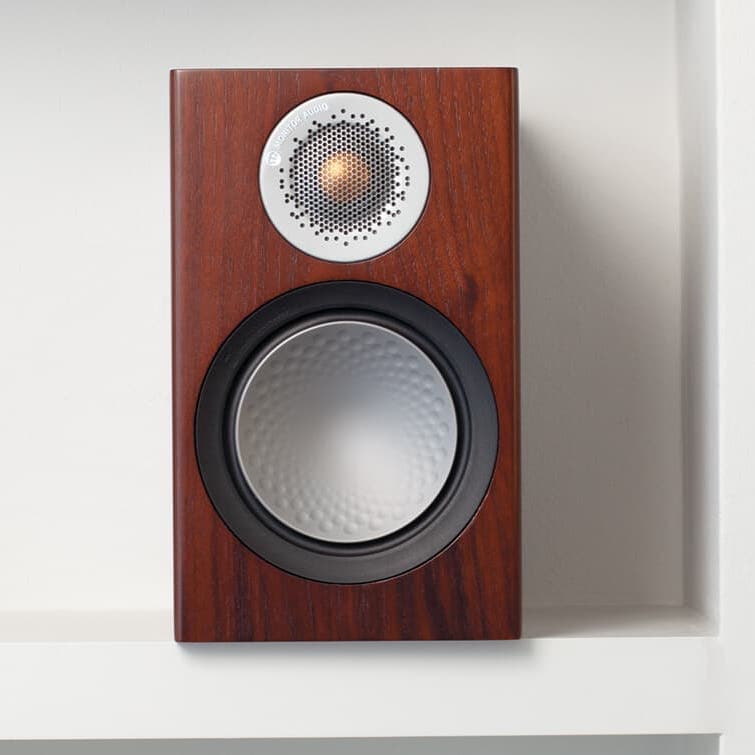 Wood-inlaid speakers sitting against a whilte wall on a white shelf.